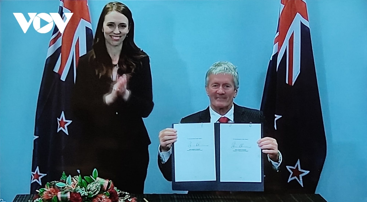 A New Zealand Minister pens the agreement in the presence of PM Jacinda Ardern