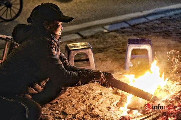 The owner of a tea shop burns a fire on the sidewalk at night.