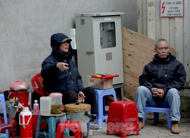 The owner of a tea shop on the pavement of Hang Bong street seeks a way to cope with the strong winds amid the extreme cold spell.