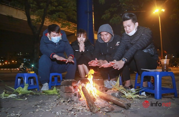 A group of youngsters sit around a bonfire outside a tea shop and enjoy the warming glow of wood burning at night.