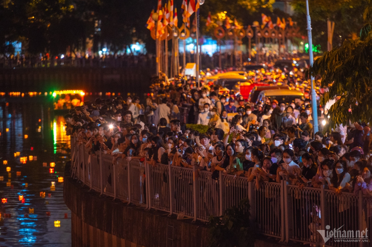 People stand along the canal as they watch the lanterns glowing in the night.