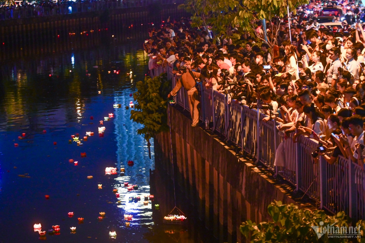 People stand along the canal watching the lanterns glowing bright in the night.