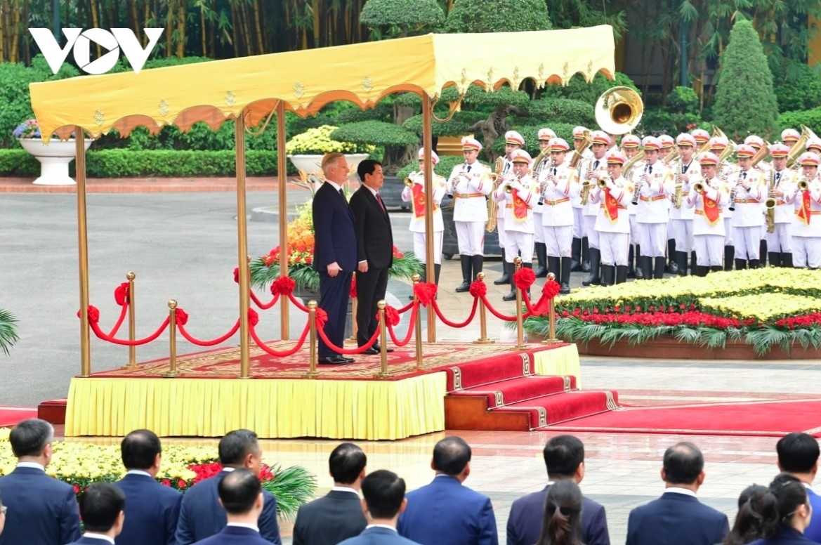 The two leaders stand on the podium while military bands play the national anthems of both nations.