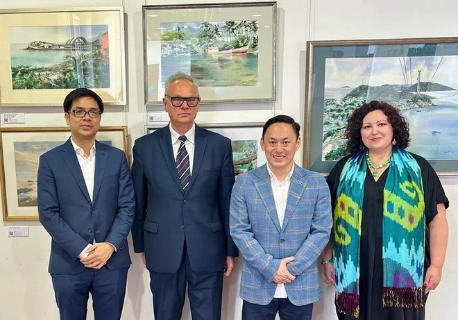 Painter Minh Dam (second from right) takes a photo with guests attending the opening ceremony of the exhibition. (Photo: anninhthudo.vn)