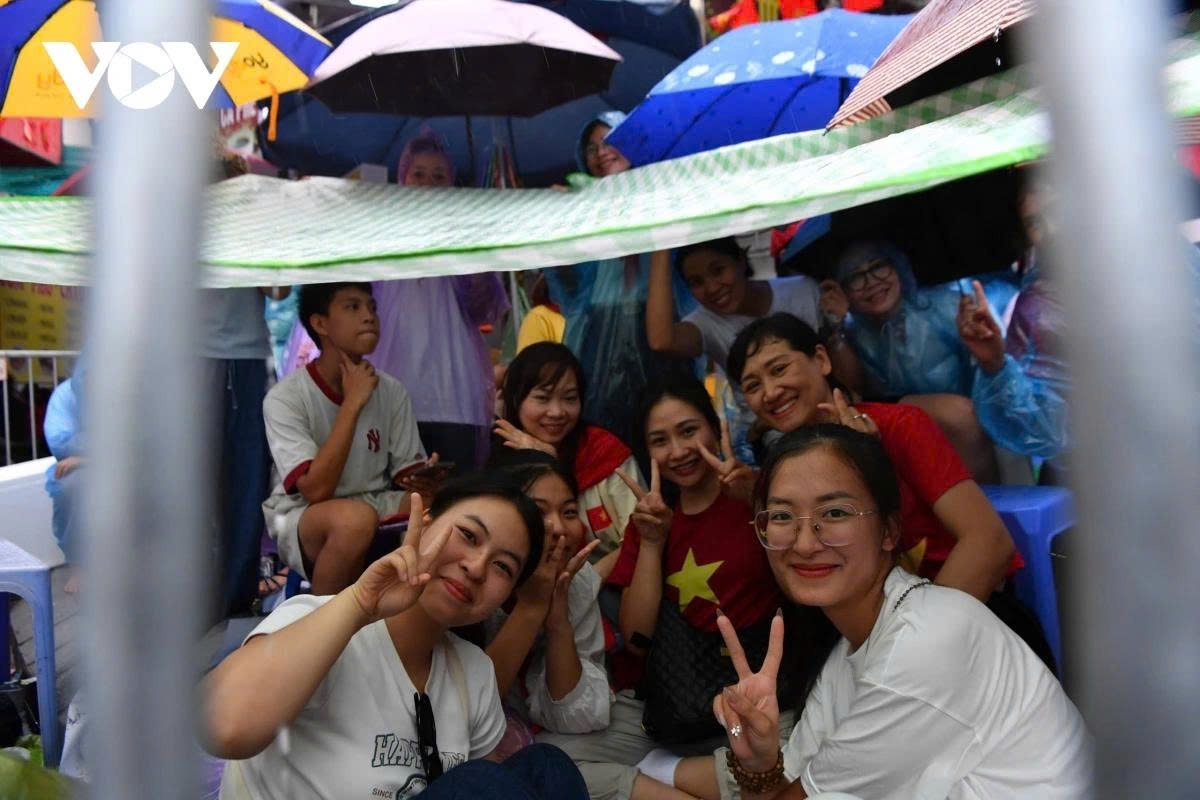 By around 2 p.m., thunderstorms appear in many areas of Hanoi. Residents, equipped with umbrellas, tarps, and raincoats, stand in the rain to hold their spots for watching the rehearsal.