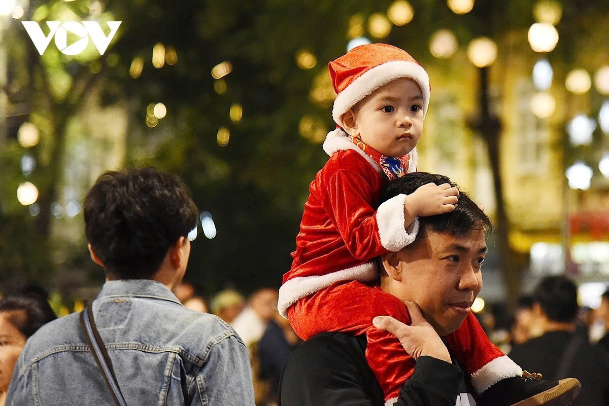 A man carries a baby dressed as Santa Claus, adding to the festive atmosphere in front of Hanoi Cathedral.