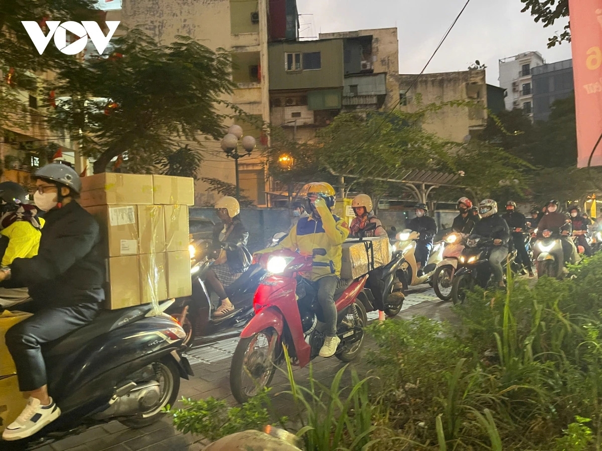 Prolonged congestion at the Le Van Luong - Nguyen Trai intersection has left car lanes nearly full, forcing many motorbikes onto sidewalks in search of an escape route. Some riders are seen cautiously moving through pedestrian areas to bypass the extended traffic jam.