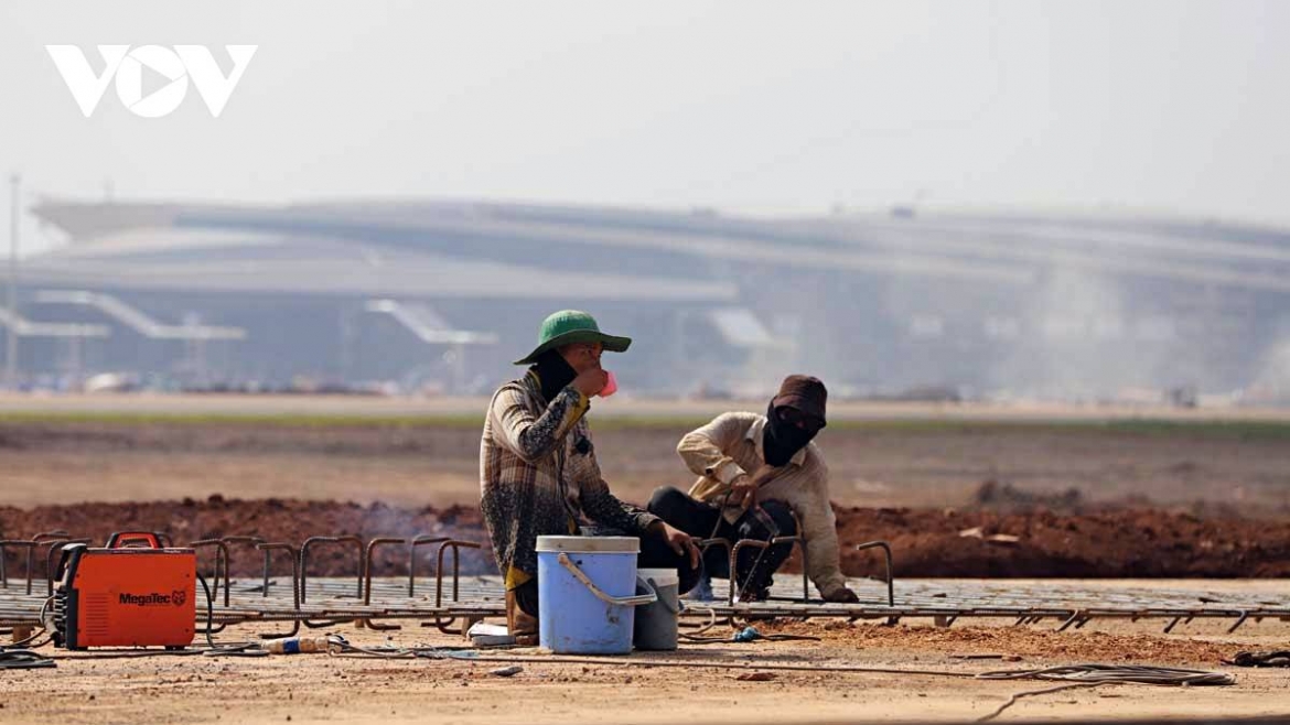 A construction worker lowers his mask, his face darkened by sun and dust, taking a moment to drink water at the Long Thanh airport site.