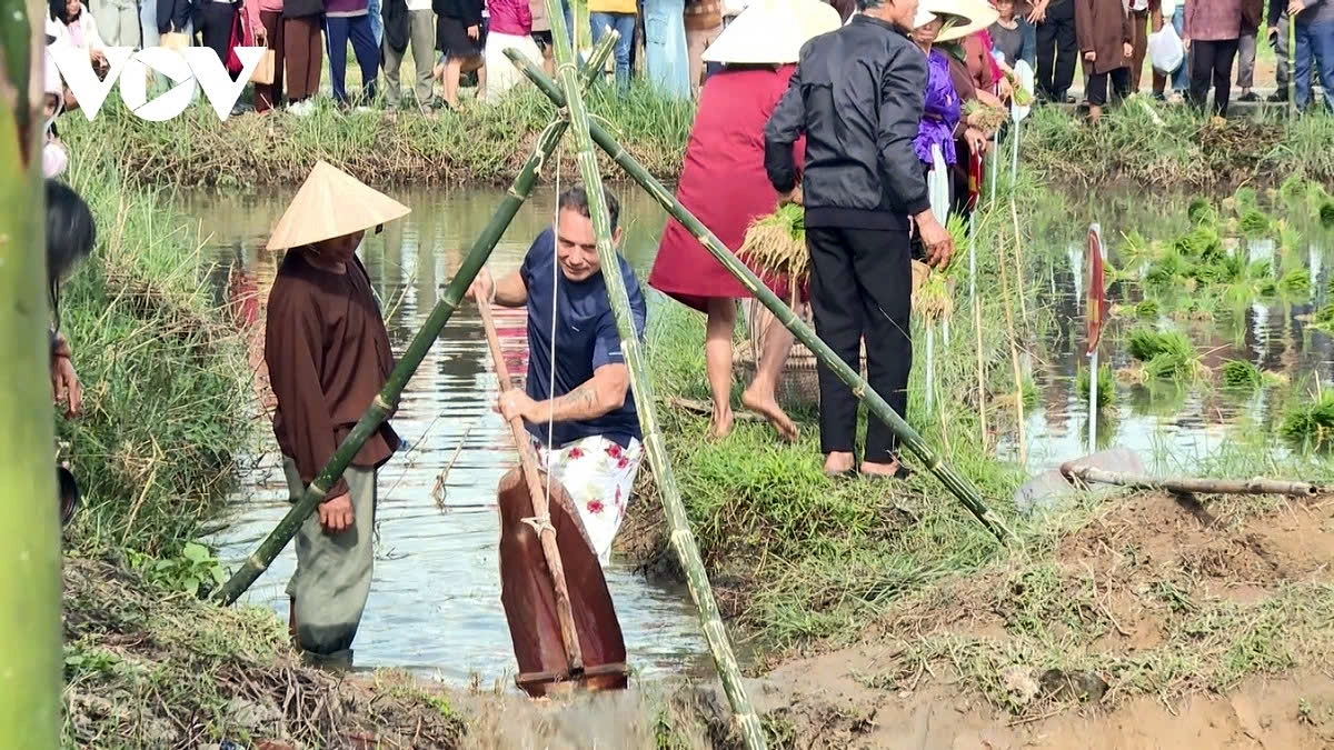 An international tourist learns how to scoop water and catch fish in the rice field