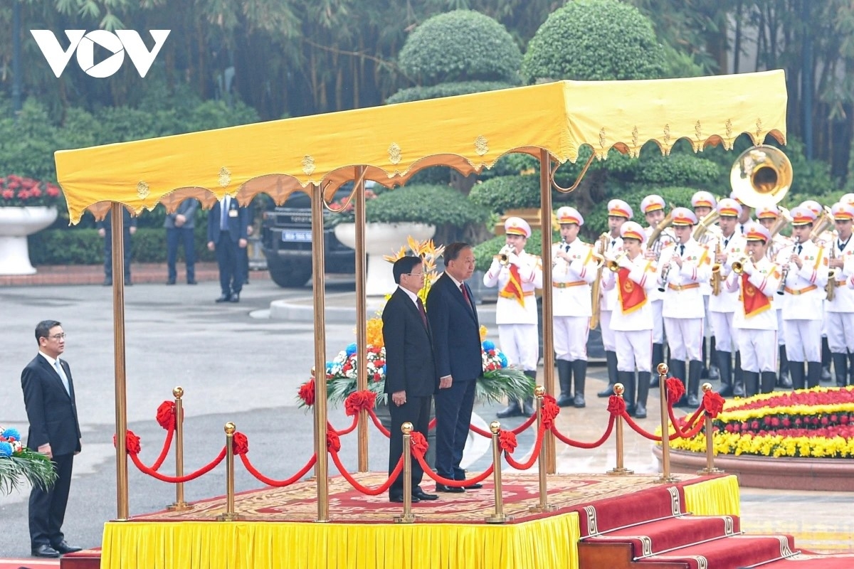 Party General Secretary To Lam invites top Lao leader Thongloun Sisoulith to the podium of honour to render the flag salute.