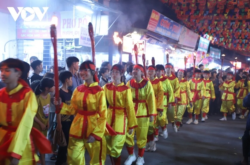 A winding line of people carrying torches glows through the night, like a fire dragon moving across the heritage site.