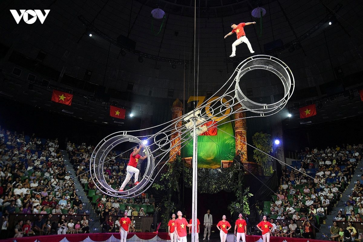 Artists in red costumes perform a demanding circus stunt on stage, adding a striking visual expression of national pride to the performance.